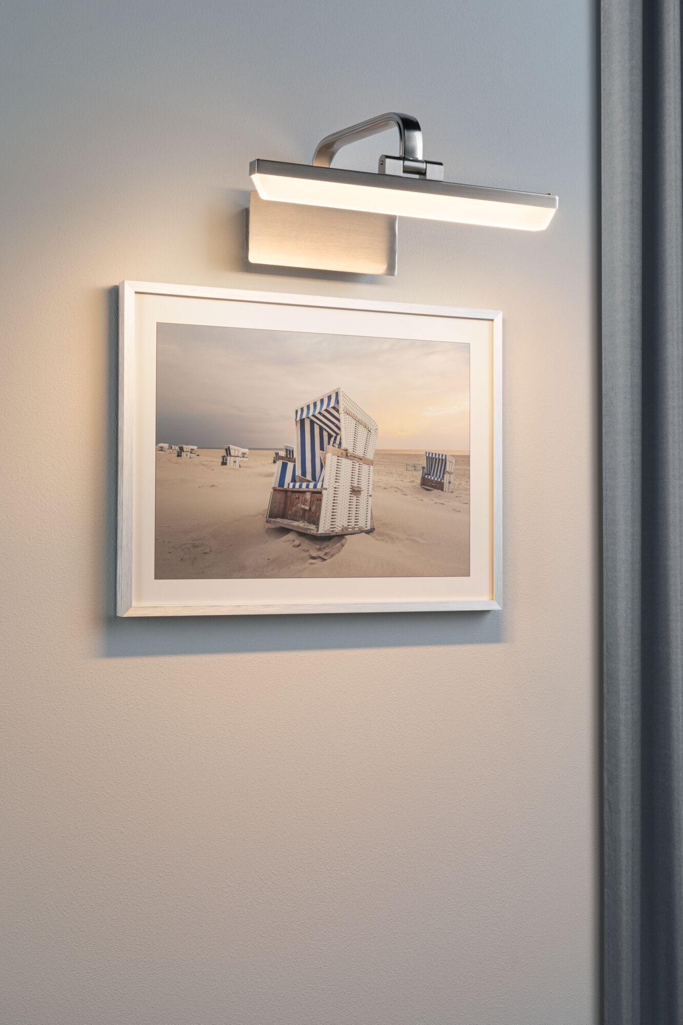 Modern brushed metal wall lamp with warm white LED light above a beach chair photo.
