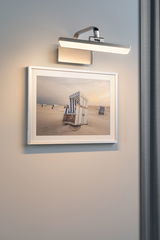 Modern brushed metal wall lamp with warm white LED light above a beach chair photo.
