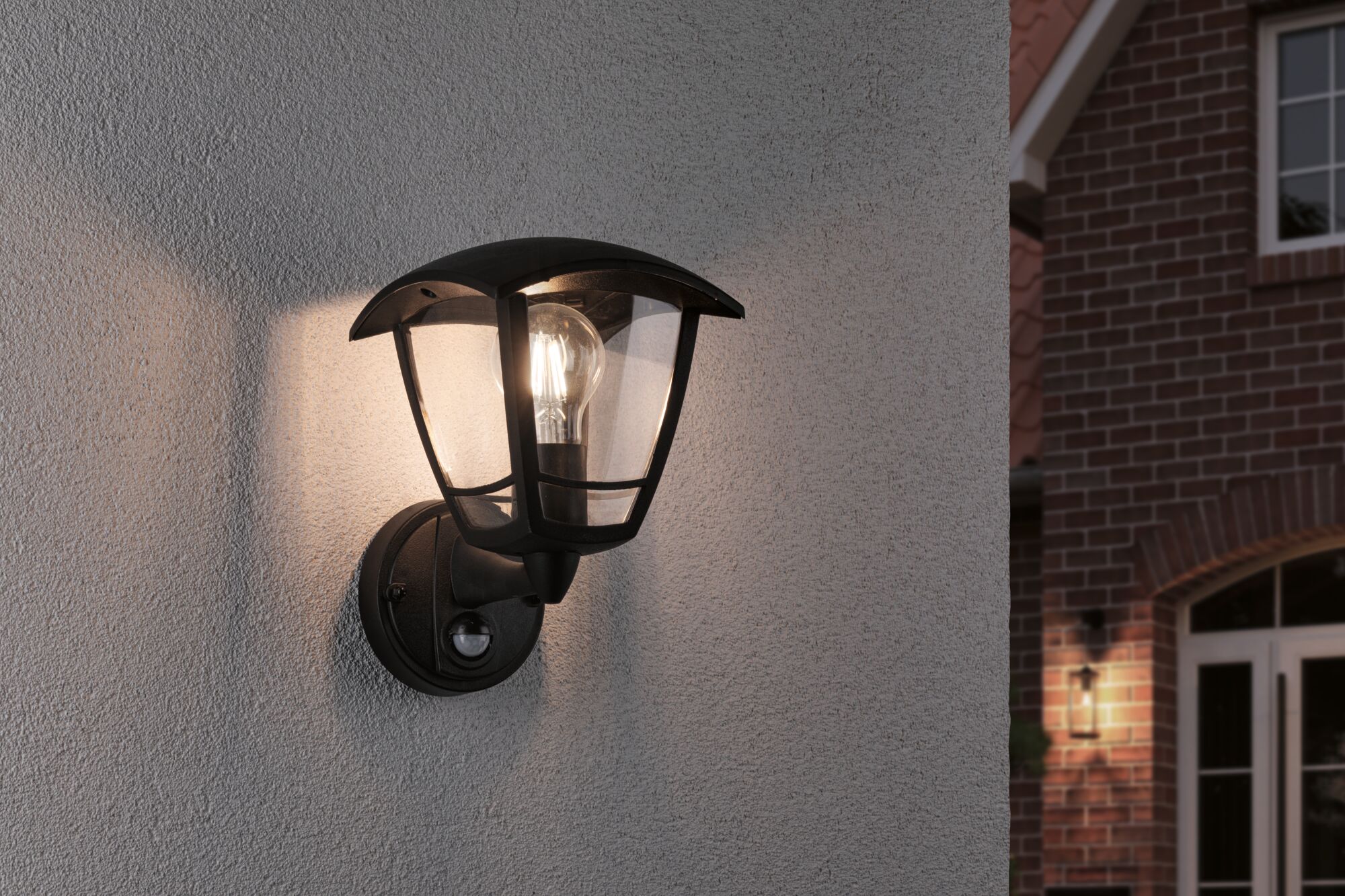 Schwarze Außenwandleuchte aus Metall mit klarem Glas und Bewegungsmelder an Hauswand beleuchtet Eingangsbereich