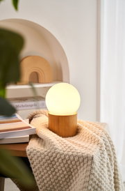 Moderne Tischleuchte mit Holzsockel und milchigem Glas in warmweißem Licht für gemütliche Wohnräume