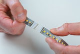 Zwei Hände verbinden LED-Streifen mit gelben LEDs und Metallkontakten für flexible Beleuchtungslösung