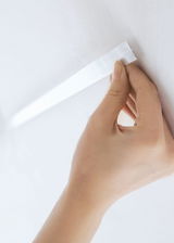 Hand attaching white adhesive tape to wall for LED strip light installation and lighting solution