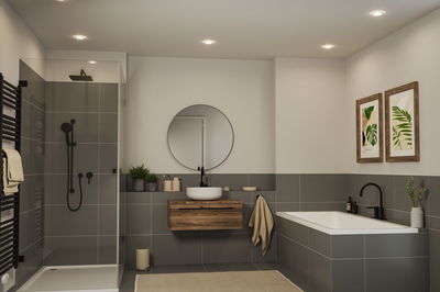 Modernes Badezimmer mit grauen Fliesen, Holz-Waschtisch, runder Spiegel und schwarzer Armatur für Badewanne und Dusche