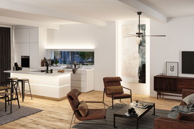 Salon moderne avec fauteuils en tissu marron, sol en bois et îlot de cuisine blanc avec éclairage LED