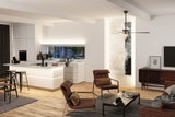 Modern living room with brown fabric armchairs, wooden floor and white kitchen island with LED lighting
