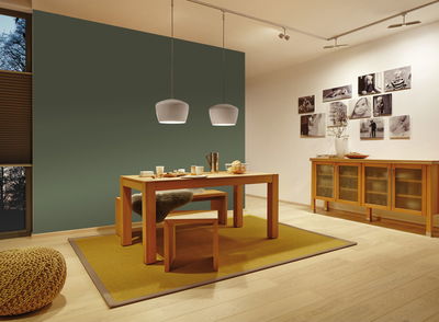 Modern dining room with wooden table and bench on yellow rug, white pendant lights and photo wall.