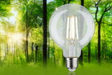 Clear glass LED bulb with visible filaments against green forest background for energy-saving lighting