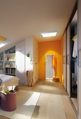 Modern bedroom with light wood floor and square ceiling light providing warm illumination