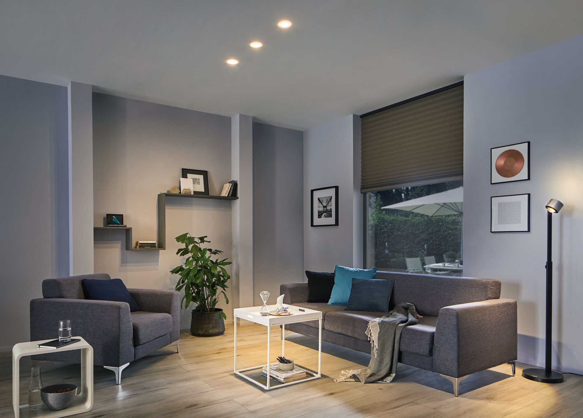 Modern living room with grey fabric sofa, armchair, white side table and black floor lamp with warm LED light.