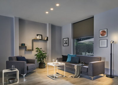 Modernes Wohnzimmer mit grauem Stoffsofa, Sessel, weißem Beistelltisch und schwarzem Stehlampe mit warmem LED-Licht.