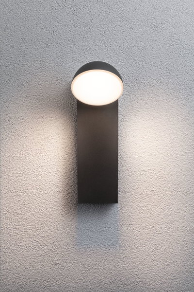 Modern black wall light with round white diffuser on textured wall, LED outdoor lighting fixture