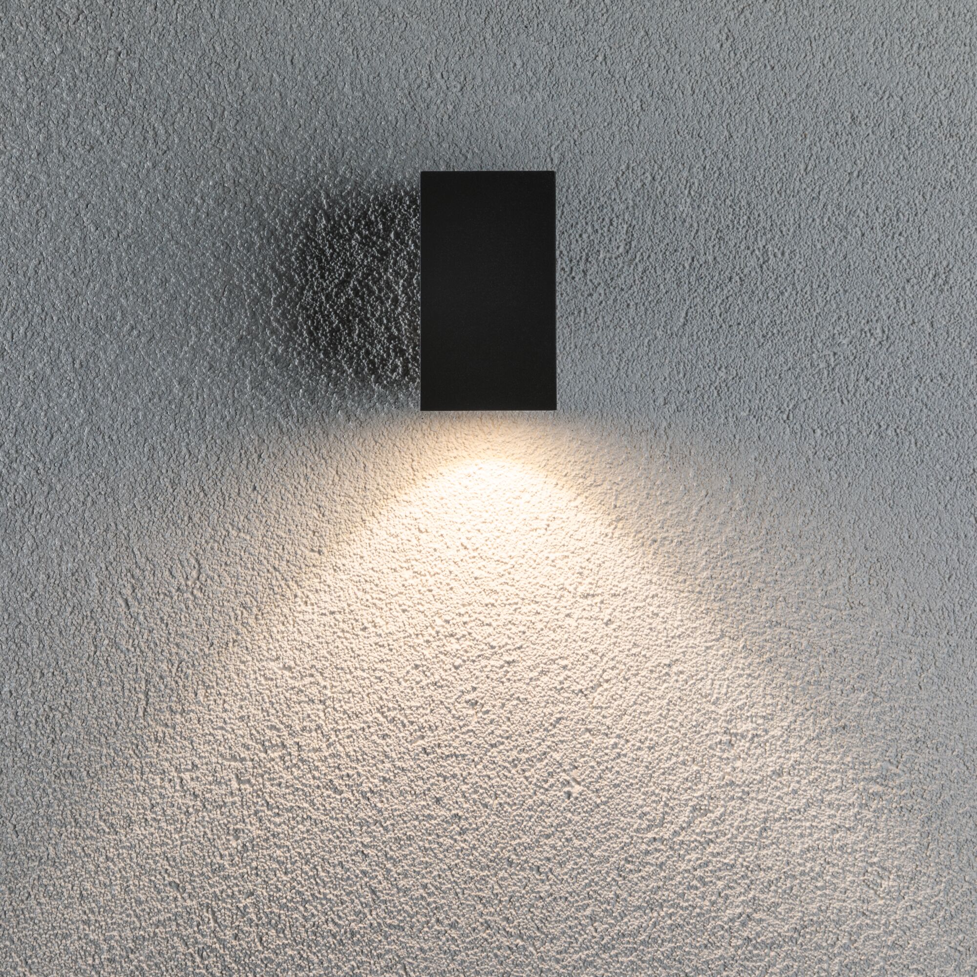 Black rectangular metal LED wall light with warm white illumination on textured wall