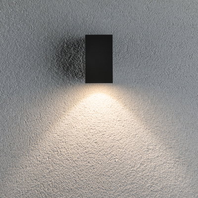Zwarte rechthoekige metalen wandlamp met warm wit licht op een grijze gestructureerde muur