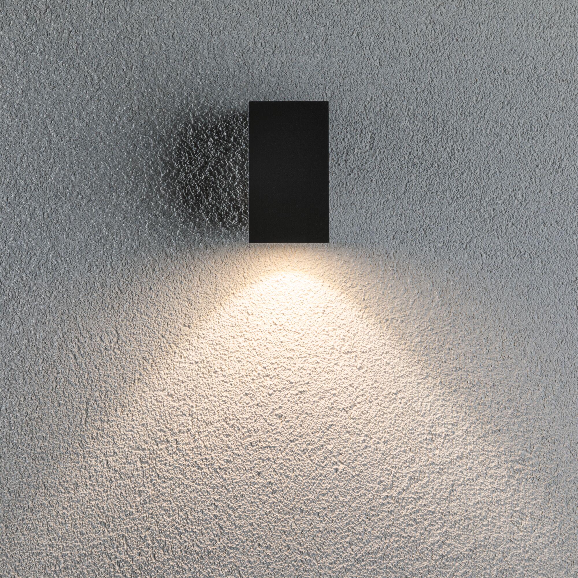 Black rectangular metal wall light with warm white illumination on textured grey wall