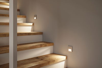 Moderne Treppenbeleuchtung mit weißen LED-Wandeinbauleuchten und Holzstufen für sicheres Gehen