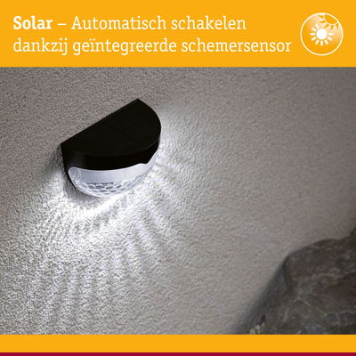 Zwarte solar wandlamp met geïntegreerde schemersensor die wit licht op een gestructureerde muur werpt