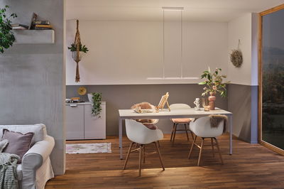 Modern dining area with white table, wooden chairs, and minimalist LED pendant light emitting warm light.