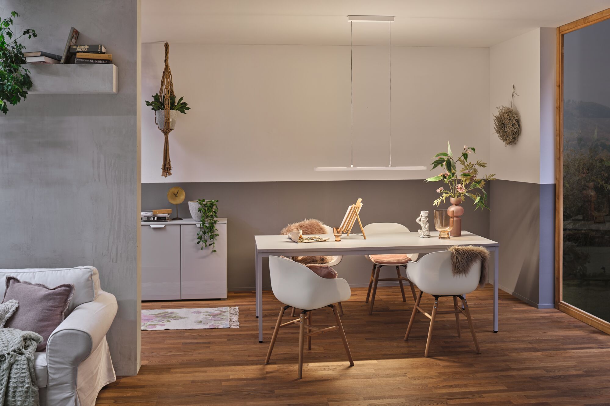 Salle à manger moderne avec table blanche, chaises en bois et suspension LED minimaliste à lumière chaude.