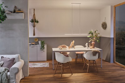 Moderner Essbereich mit weißem Tisch, Holzstühlen und minimalistischer LED-Pendelleuchte in warmem Licht.