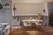 Modern dining area with white table, wooden chairs, and minimalist LED pendant light emitting warm light.