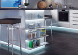 Modern white kitchen island with illuminated shelves, black bar stools, and grey tiled floor