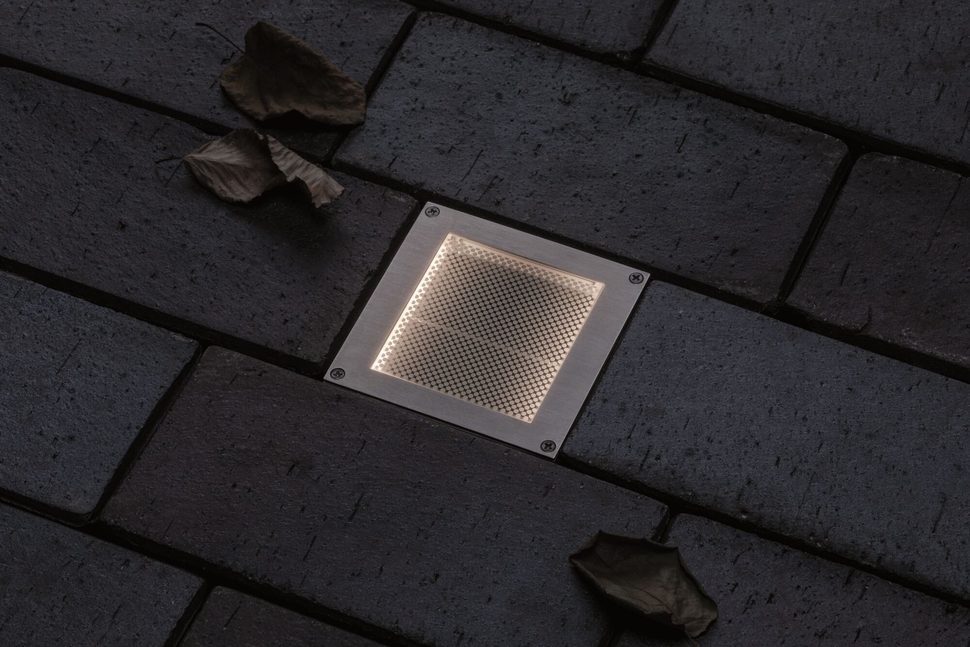 Eingelassene quadratische LED-Bodenleuchte aus Edelstahl mit warmweißem Licht auf dunklem Pflaster