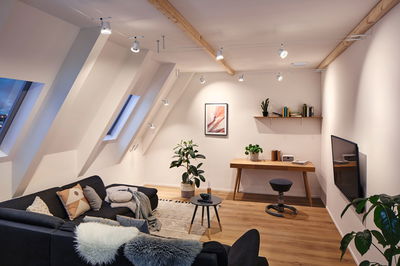 Salon moderne avec canapé noir, sol en bois et spots LED blancs suspendus au plafond pour éclairage d'accent