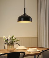 Zwarte metalen hanglamp met warm licht boven houten tafel met borden en bloemenvaas