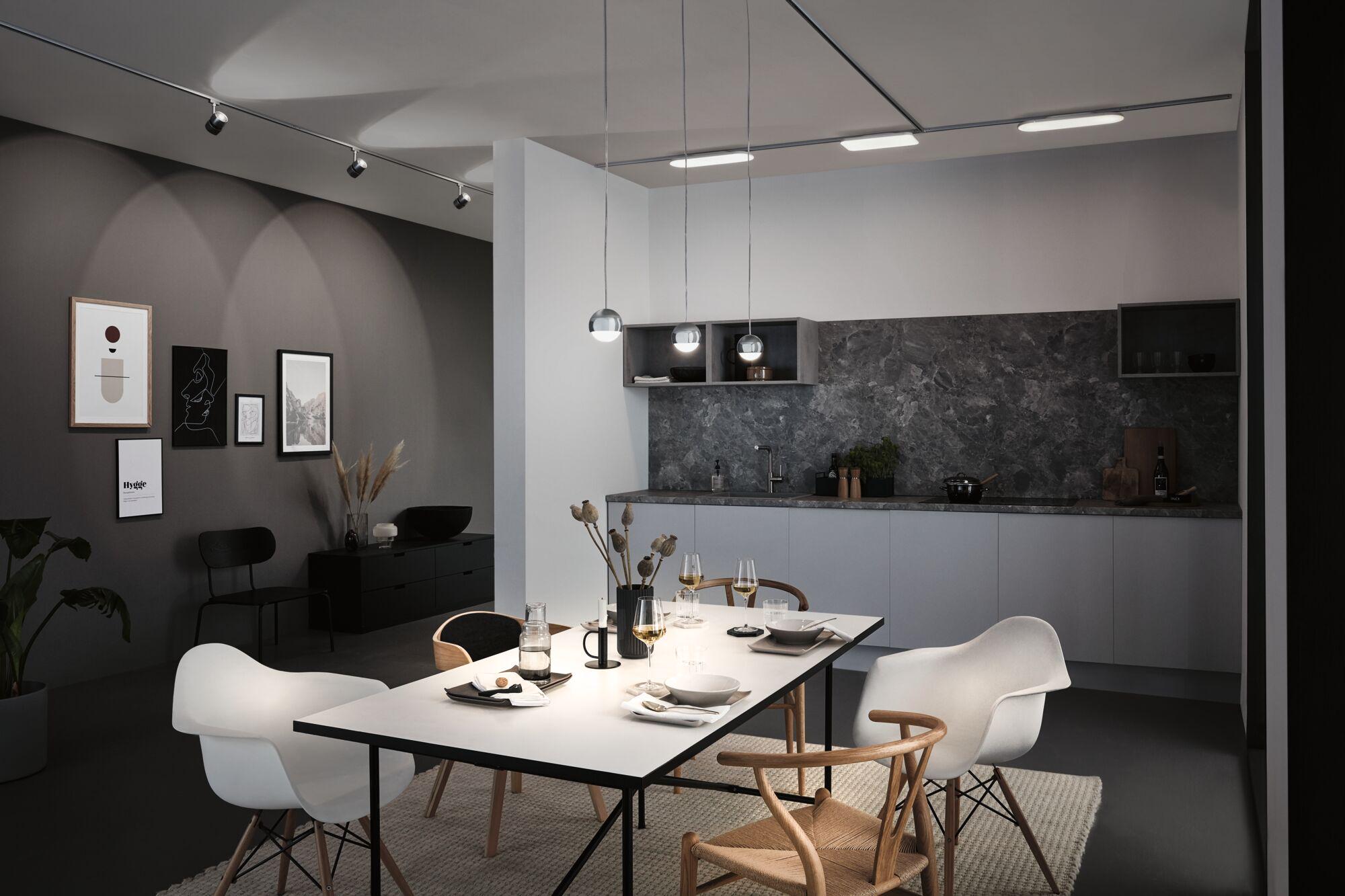 Éclairage de salle à manger moderne avec trois suspensions rondes chromées au-dessus d'une table blanche et chaises en bois.