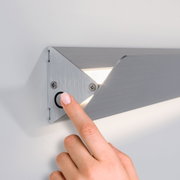 Hand pressing black button on brushed aluminium wall light with LED illumination