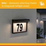 Solar-powered house number 79 with integrated twilight sensor and black frame mounted on grey wall