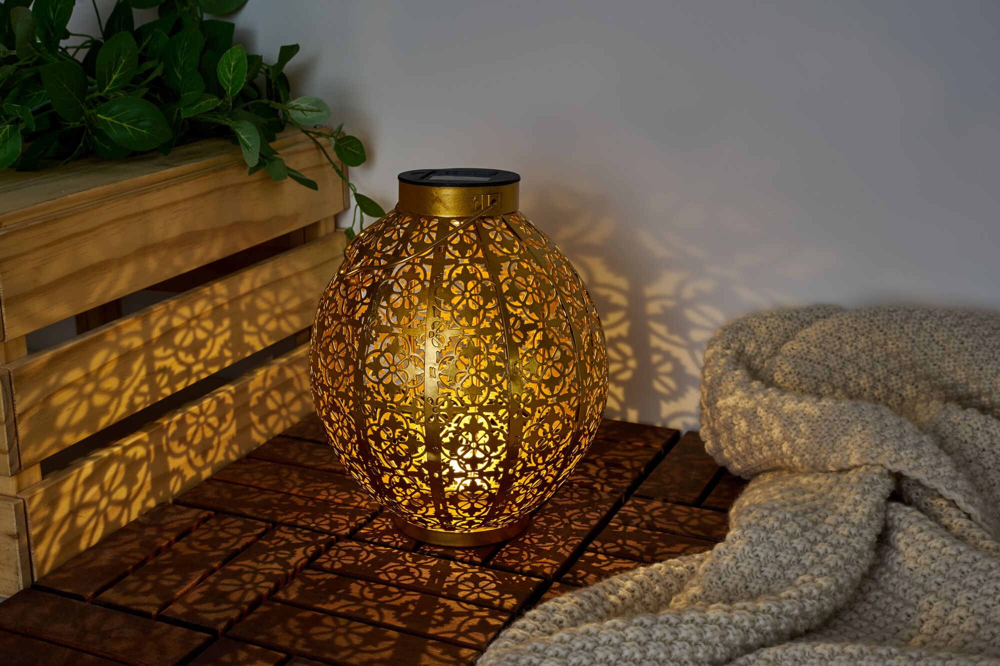 Gold metal lantern with intricate pattern casting decorative shadows on wood and wall.