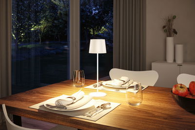 Lampe de table blanche en métal sur table en bois avec couverts et pommes dans le salon.