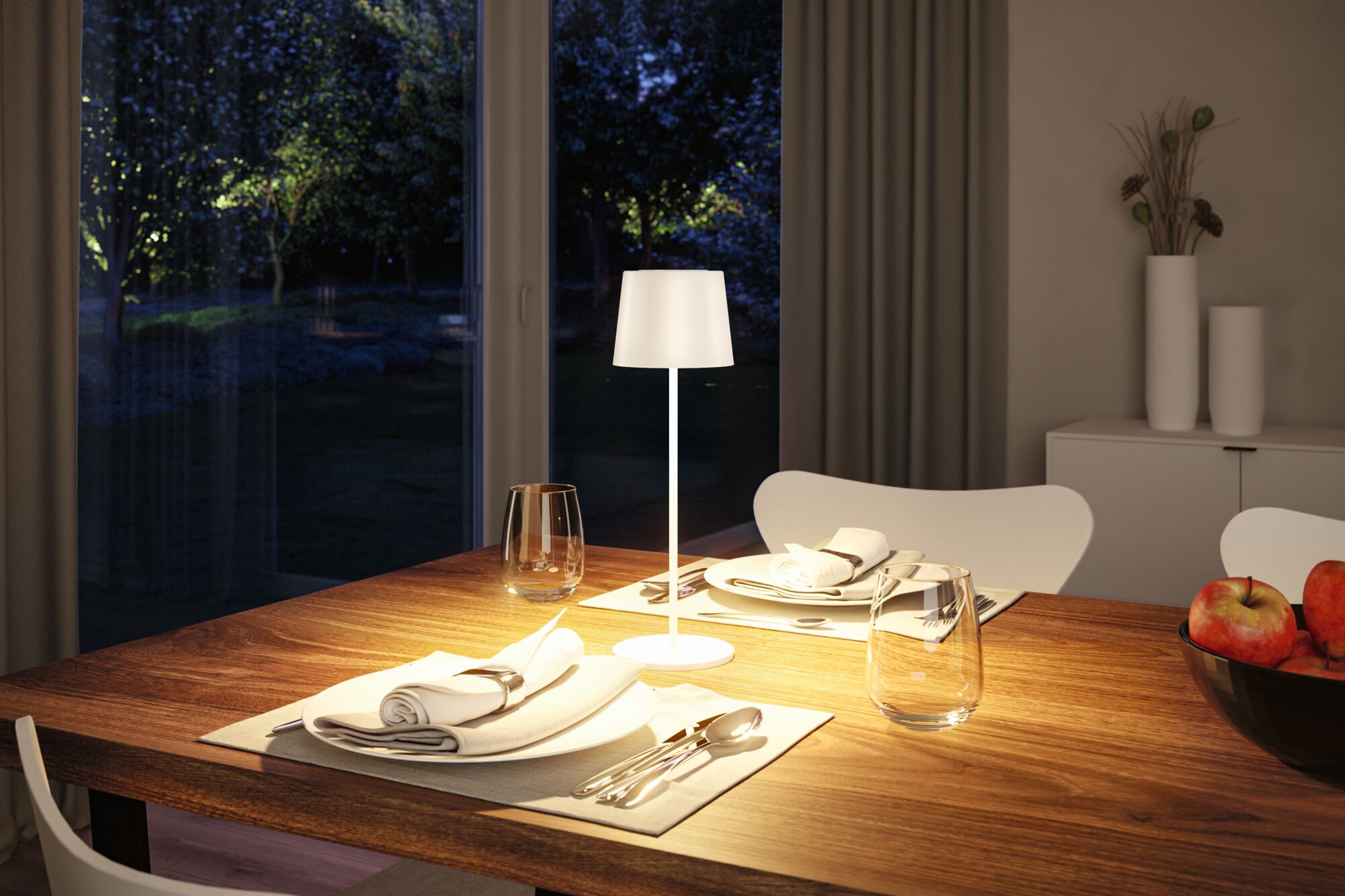 White metal table lamp on wooden dining table with set places and apples in living room.