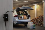 Détecteur de mouvement noir en plastique fixé sur mur en bois dans garage avec coffre de voiture ouvert et bois empilé.