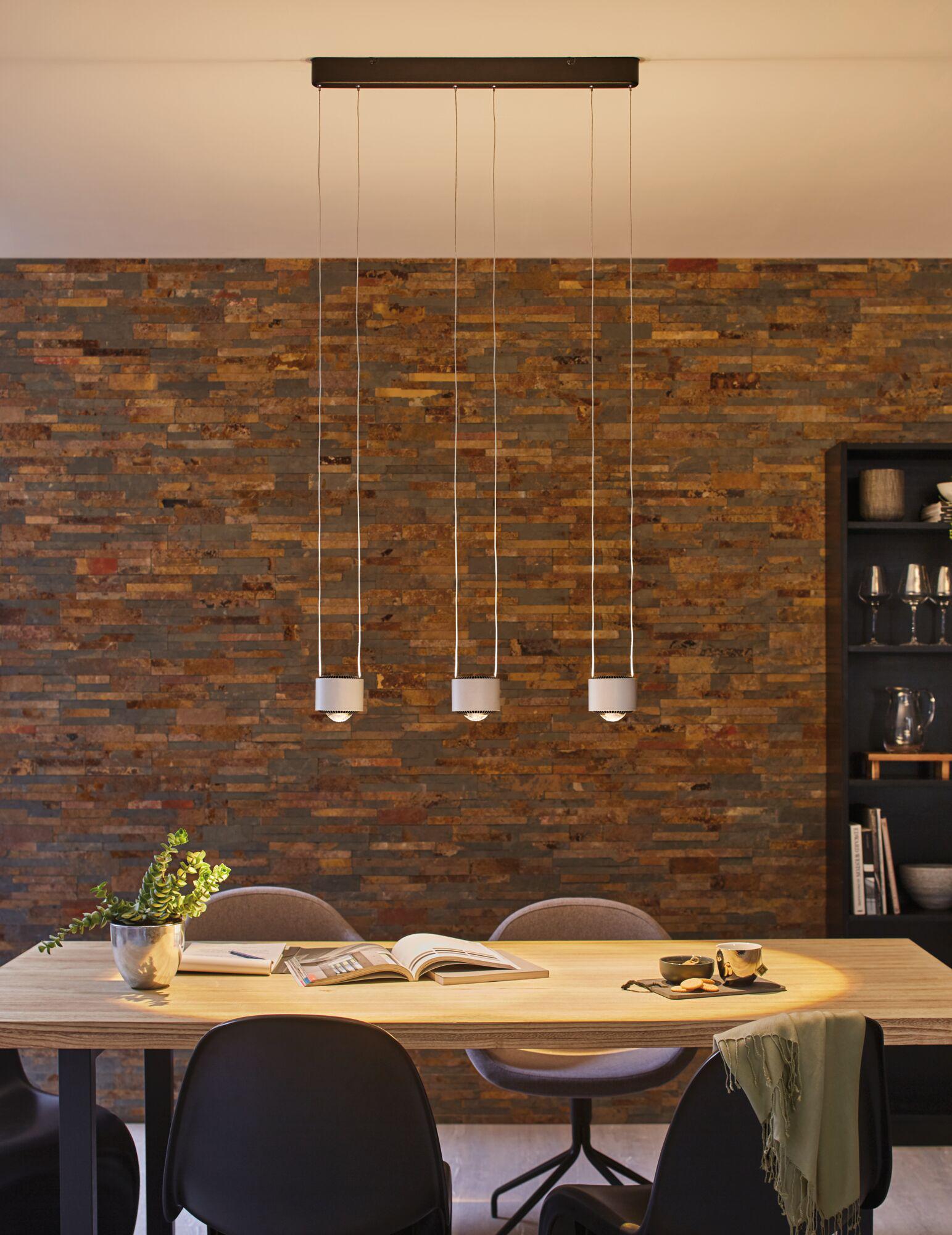 Three white metal pendant lights above light wooden table with brown stone wall in dining room