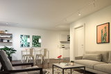 Modern living room with beige sofa, plants, white dining table, and LED spot lighting on ceiling.