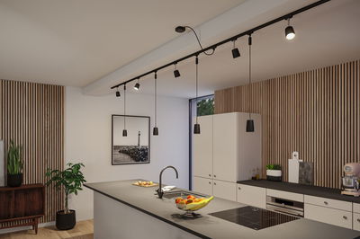 Modern kitchen with black countertop, white cabinets, and black pendant lights on track lighting system.