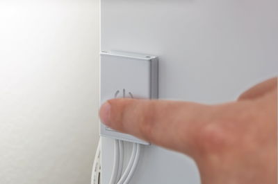 Finger trykker på sølvfarvet vægkontakt med tænd/sluk-symbol og hvide kabler til lysstyring