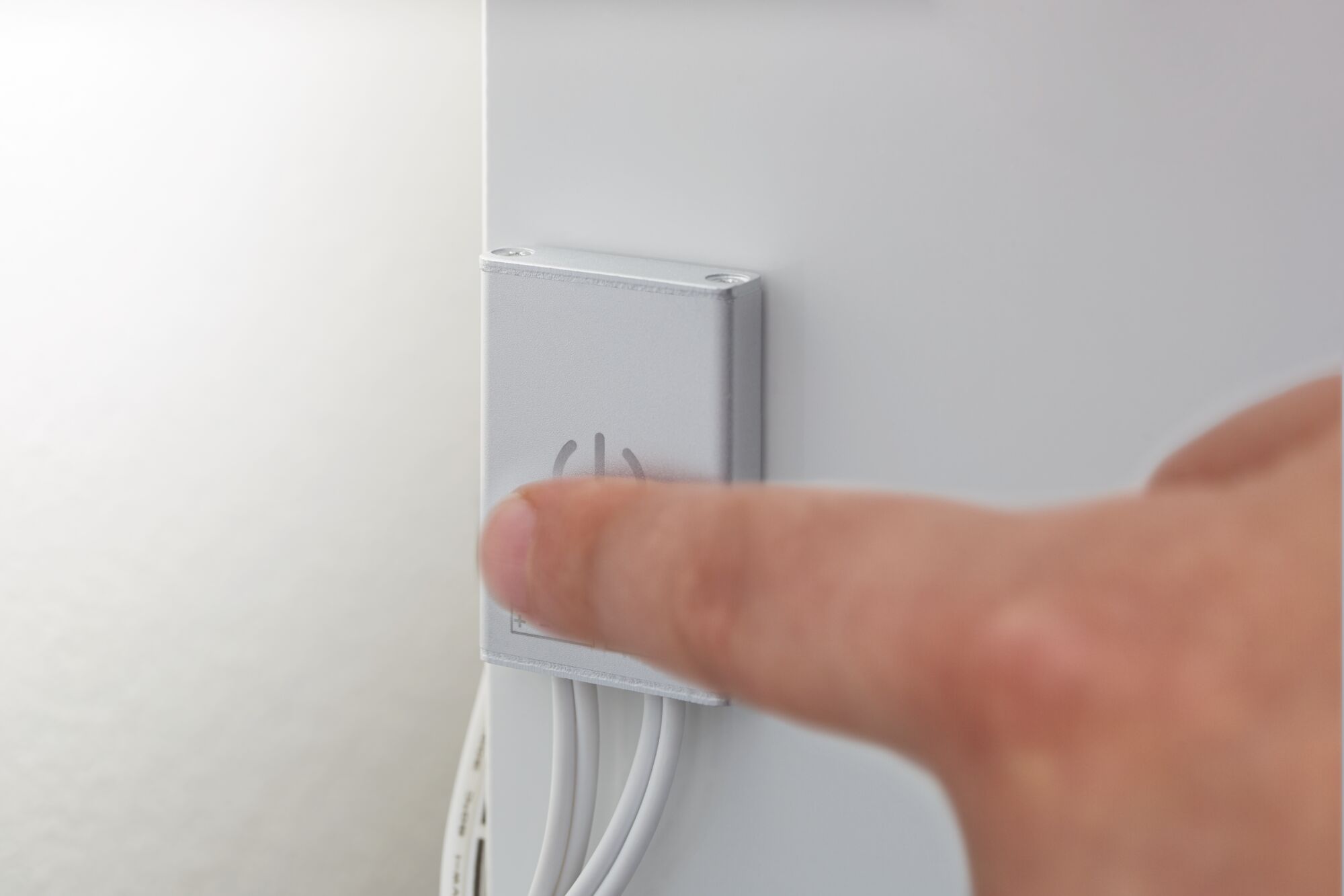 Finger trykker på sølvfarvet vægkontakt med tænd/sluk-symbol og hvide kabler til lysstyring