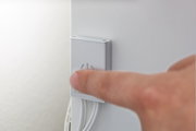 Vinger drukt op witte kunststof aan/uit-schakelaar met stroomsymbool aan muur met kabels