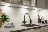 Modern kitchen countertop with black sink, matte black faucet, and LED under-cabinet lighting.