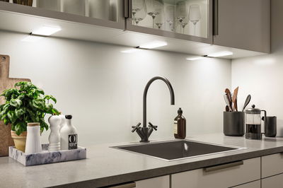 Modern kitchen countertop with black sink, matte black faucet, and LED under-cabinet lighting.