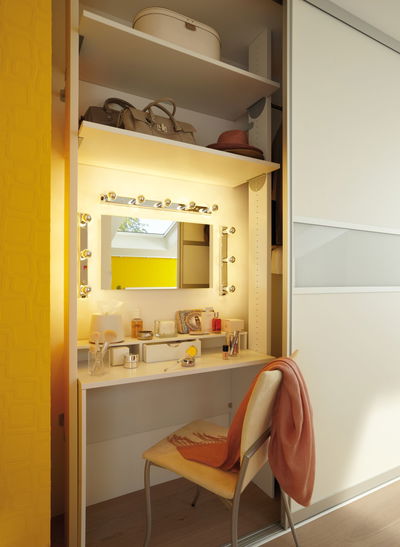 Coiffeuse blanche avec miroir éclairé et cosmétiques dans une pièce moderne avec mur jaune.