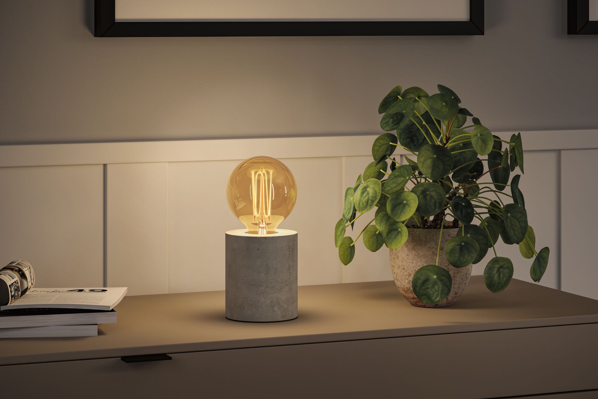 Moderne bordlampe med grå betonfod og varmt hvidt LED-pæreslys på skænk.