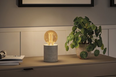 Moderne bordlampe med grå betonfod og varmt hvidt LED-pæreslys på skænk.