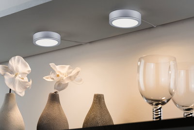Deux plafonniers LED ronds blancs en métal éclairant des vases avec orchidées blanches et verres.