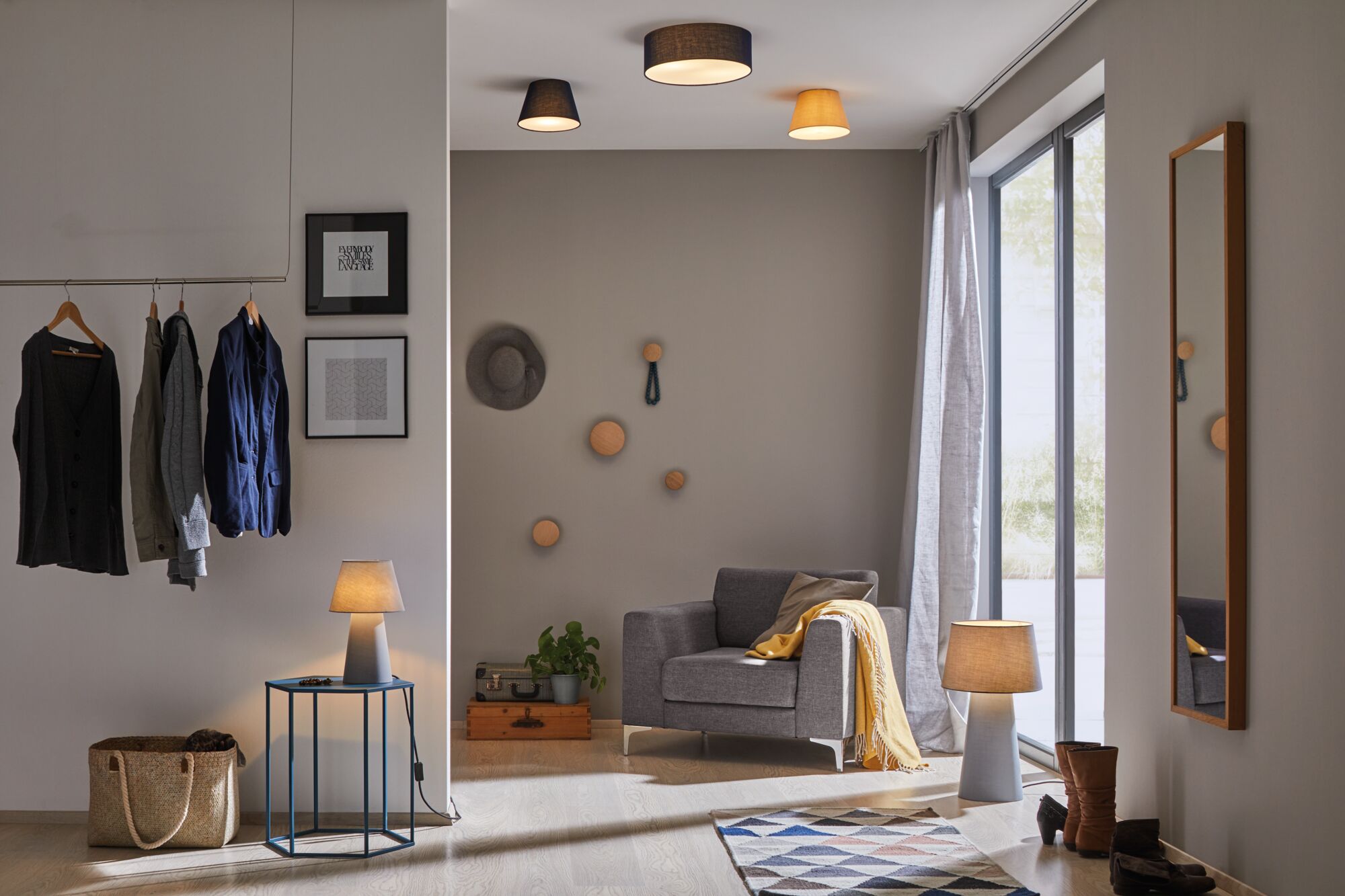 Nowoczesny salon z szarą sofą, żółtym kocem, drewnianymi lampami i wieszakiem na szarej ścianie