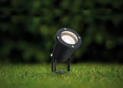 Zwarte metalen LED-buitenstraalspot op gras, weerbestendige tuinverlichting voor paden en planten.