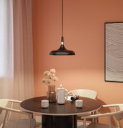 Black metal pendant lamp above round wooden table with ceramic jug and cups in dining room